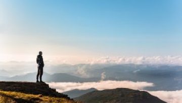 man standing at the edge of the cliff looking at mountains